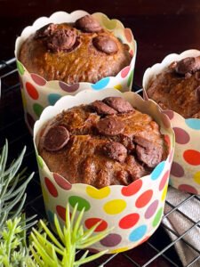 Three chocolate chip muffins in paper cups arranged neatly on a cooling rack, showcasing their delicious texture and color.